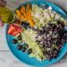A vibrant vegetable salad with olives, feta, and strawberries being drizzled with olive oil.