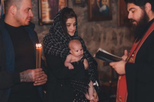 A touching moment during an Orthodox baptism ceremony with a priest, parents, and baby.