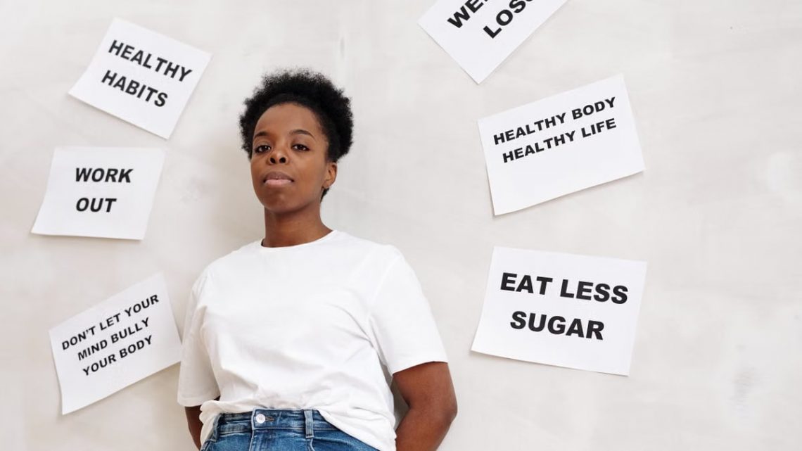 African American woman stands near motivational health slogans on the wall, promoting a positive lifestyle.